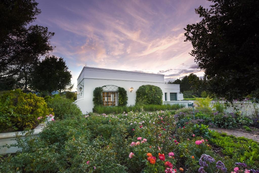 a white house with a garden with flowers at Greenhill Farm Cape Dutch Cottage Plettenberg Bay - 1 Bedroom Private Cottage in Plettenberg Bay