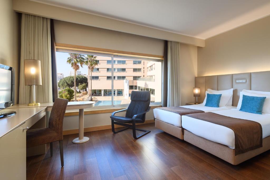 a hotel room with a bed and a desk and a window at TRYP by Wyndham Porto Expo Hotel in Leça da Palmeira