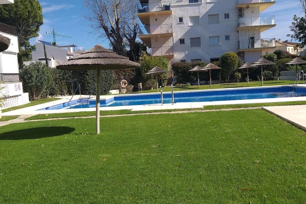 an umbrella in the grass next to a swimming pool at Apartamento en la milla de oro, a 100m de la playa in Marbella