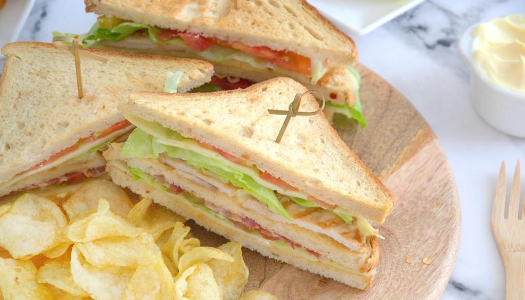a sandwich and chips on a wooden plate at Montree Phuket Hotel in Phuket Town