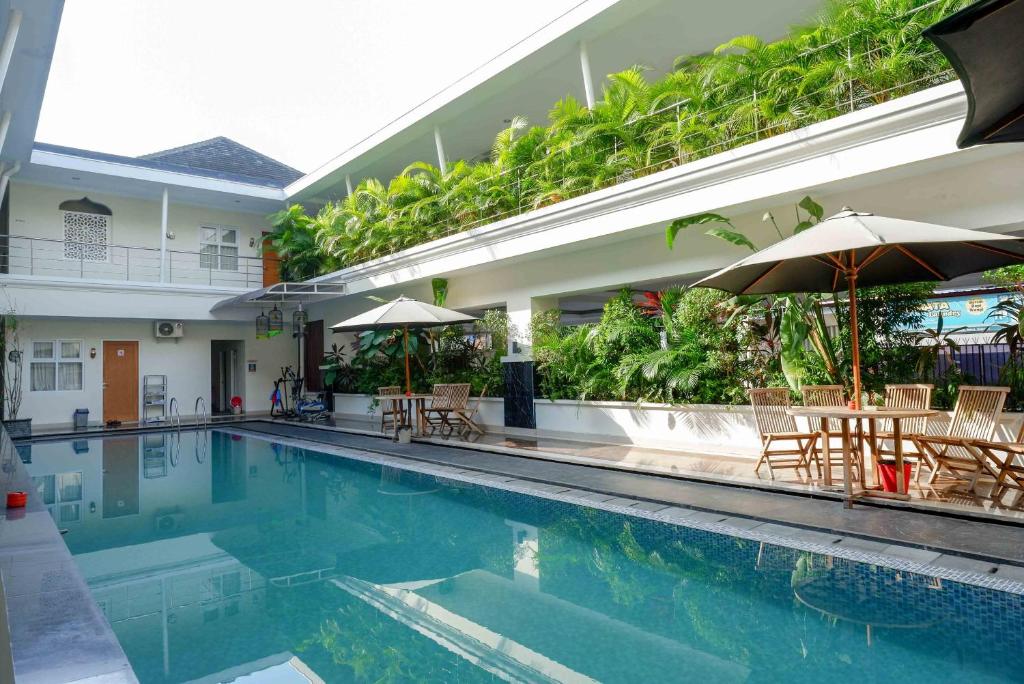 einen Pool mit Stühlen und Sonnenschirmen neben einem Gebäude in der Unterkunft Urbanview Hotel Syariah Casa Azmya Yogyakarta in Kejayan