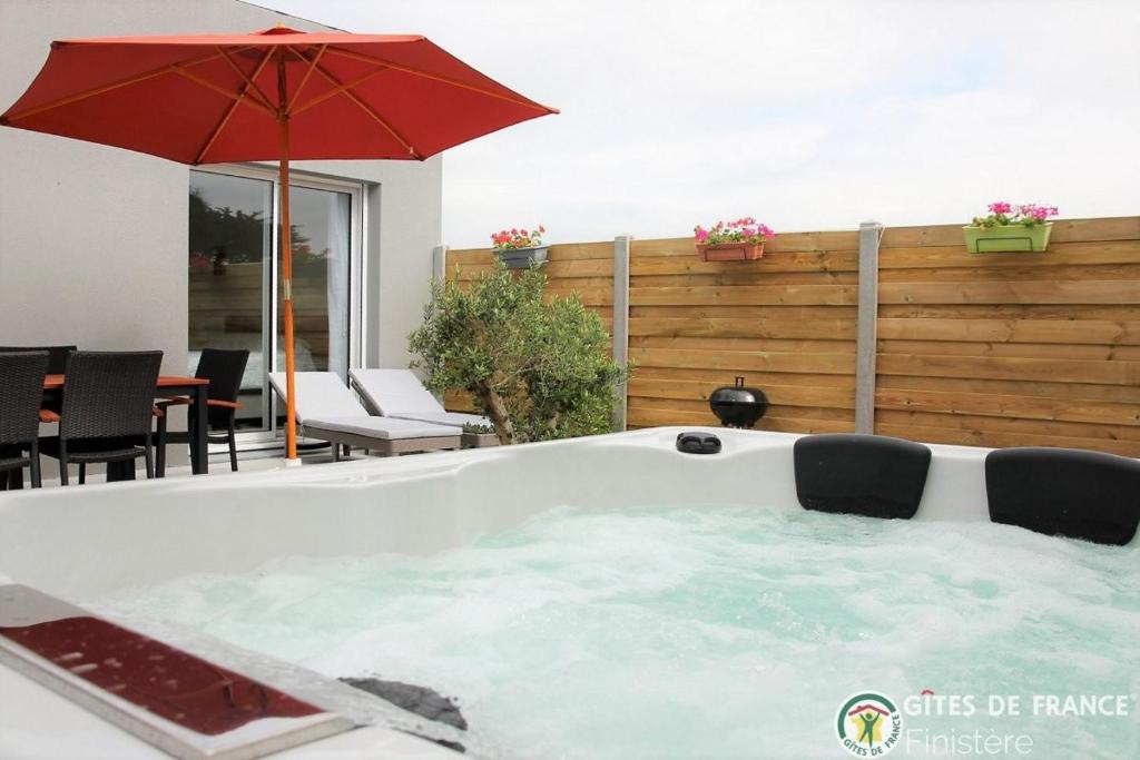 a hot tub with an umbrella on a patio at Villa le Nid Des Dunes & Spa 2 gîtes écologiques in Santec