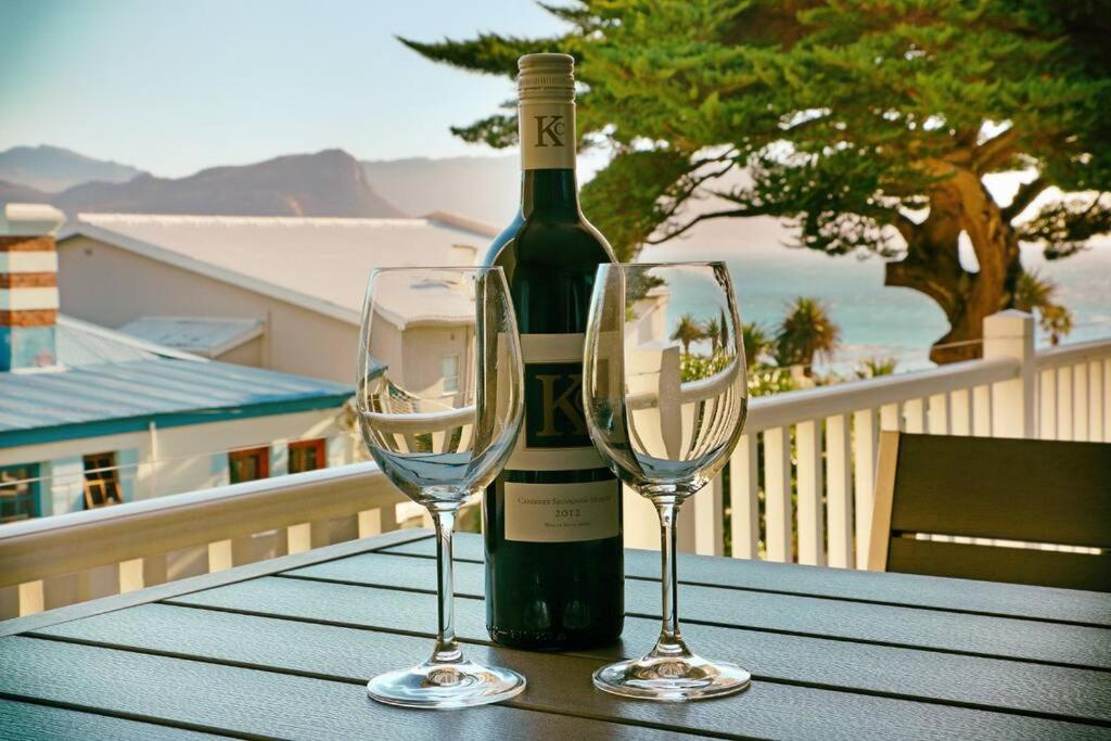 a bottle of wine and two wine glasses on a table at Penguin Haven . Luxury 2 bedroom, Boulders Beach. in Cape Town