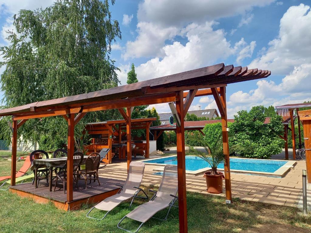 een houten paviljoen met een tafel en stoelen naast een zwembad bij Médea Apartman in Bük