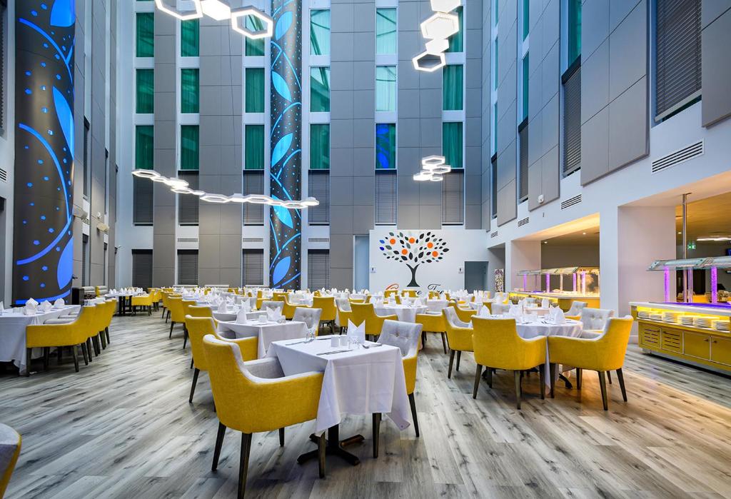 a dining room with white tables and yellow chairs at Atrium Hotel Heathrow in Hillingdon