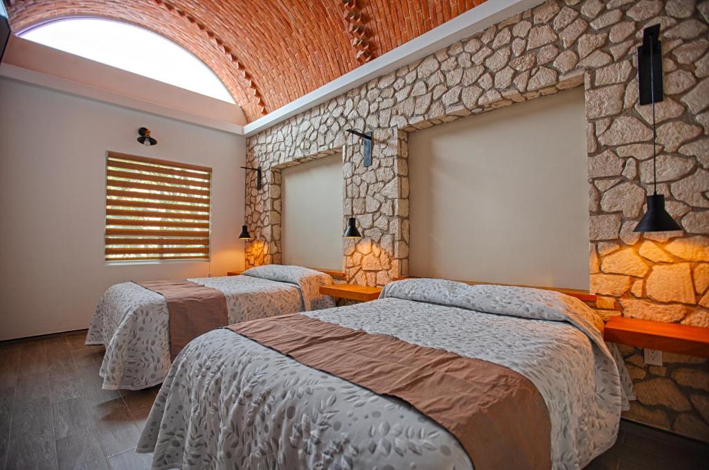 a bedroom with two beds and a stone wall at Hotel la Cuesta Toscana in Bernal