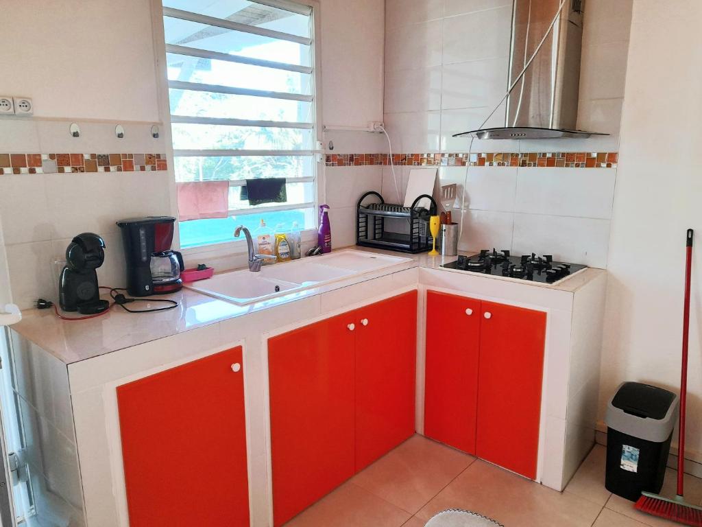 a small kitchen with red cabinets and a window at Maison charmante à Petit-Bourg avec piscine partagée in Petit-Bourg