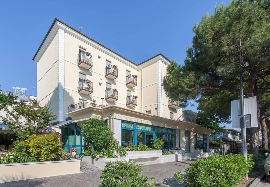 un grand bâtiment blanc dans une rue arborée dans l'établissement Hotel Rosso Blu, à Cesenatico