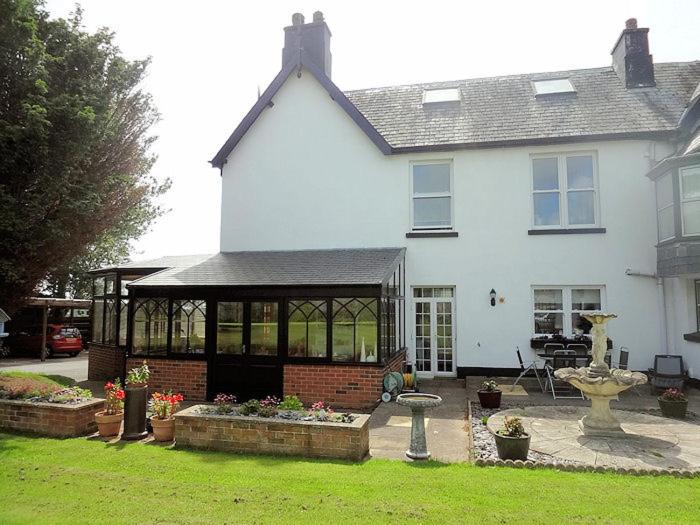 Una gran casa blanca con un patio con una fuente. en Leahurst Bed and Breakfast en Tywyn