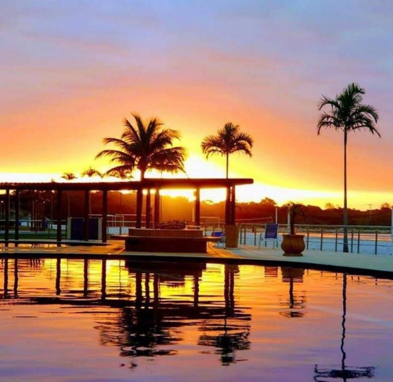uma piscina com palmeiras e o pôr-do-sol ao fundo em Resort GoldenLake em Arraial do Cabo em Arraial do Cabo