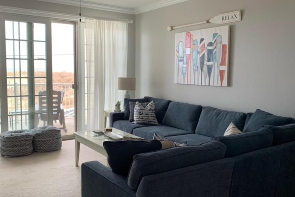 Una sala de estar con un sofá azul y una mesa. en The Sandbridge Dunes - Salty Mermaid 110, en Virginia Beach