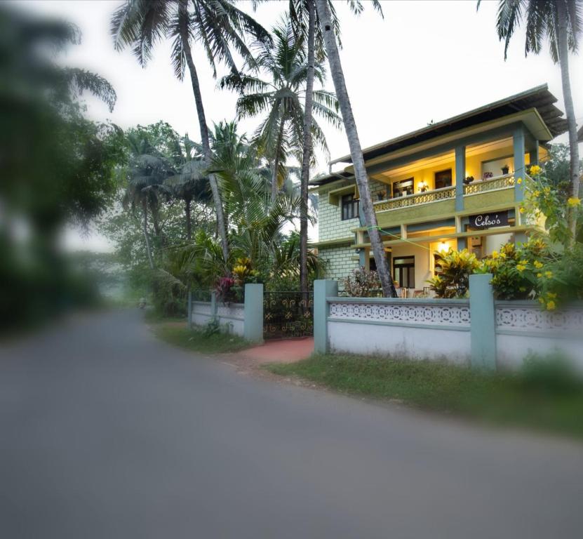 a yellow house with a white fence and palm trees at Celso's Home Stay in Panaji