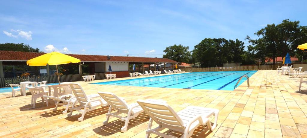 a swimming pool with white chairs and umbrellas next to a pool at Pousada Pontal de Guaratuba in Guaratuba