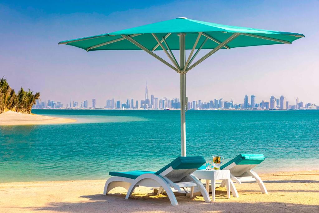 due sedie e un tavolo con ombrellone su una spiaggia di Anantara World Islands Dubai Resort a Dubai