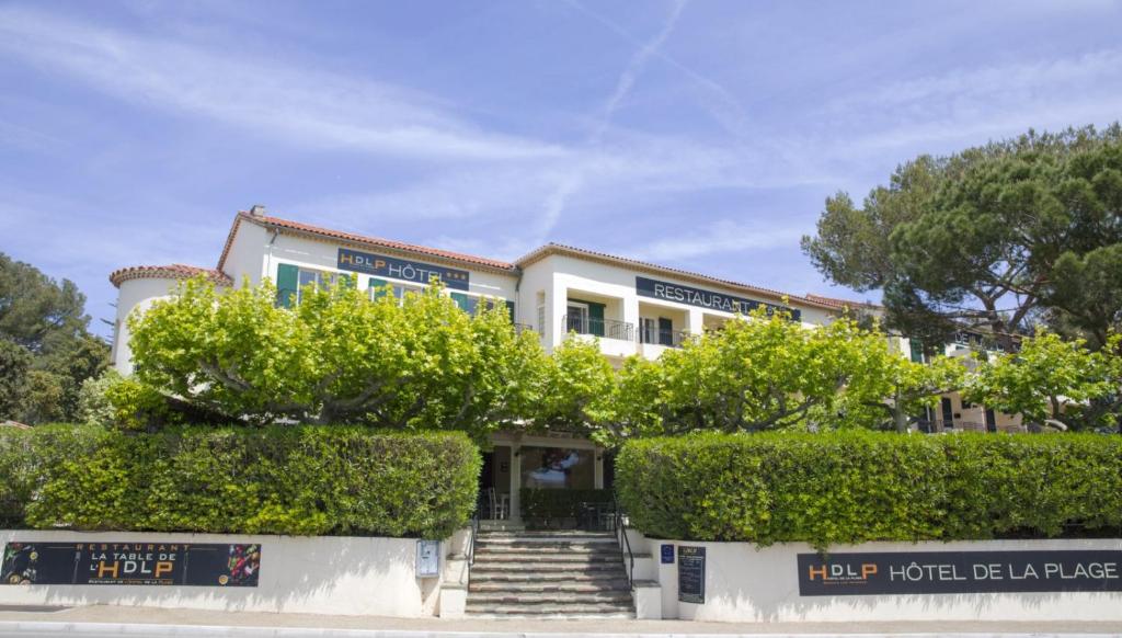 - un bâtiment blanc avec des arbres et des escaliers devant dans l'établissement Hôtel de la Plage - HDLP, à Bormes-les-Mimosas