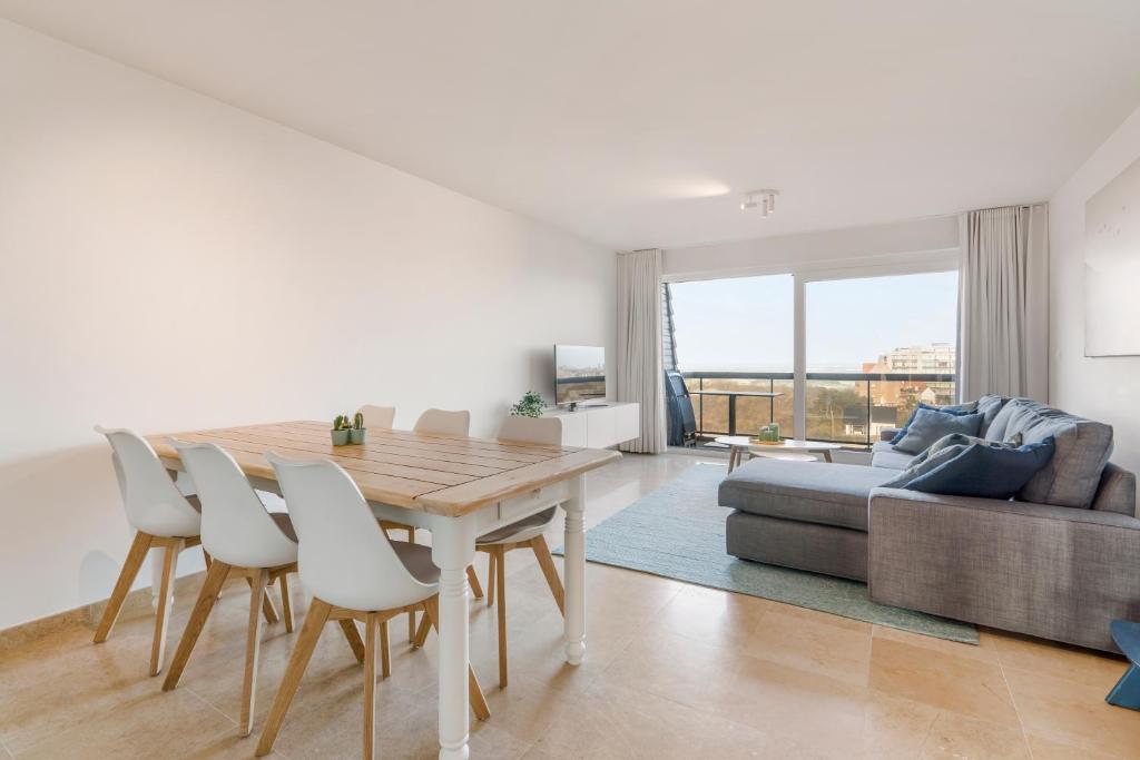 uma sala de estar branca com uma mesa de madeira e cadeiras em Ster Der Zee-Fijn app met uitgestrekt zicht op zee em Koksijde