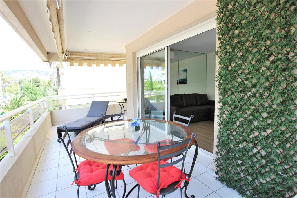 d'un balcon avec une table en verre et des chaises rouges. dans l'établissement Appartement climatisé bord de mer Palm beach avec grande terrasse, à Cannes