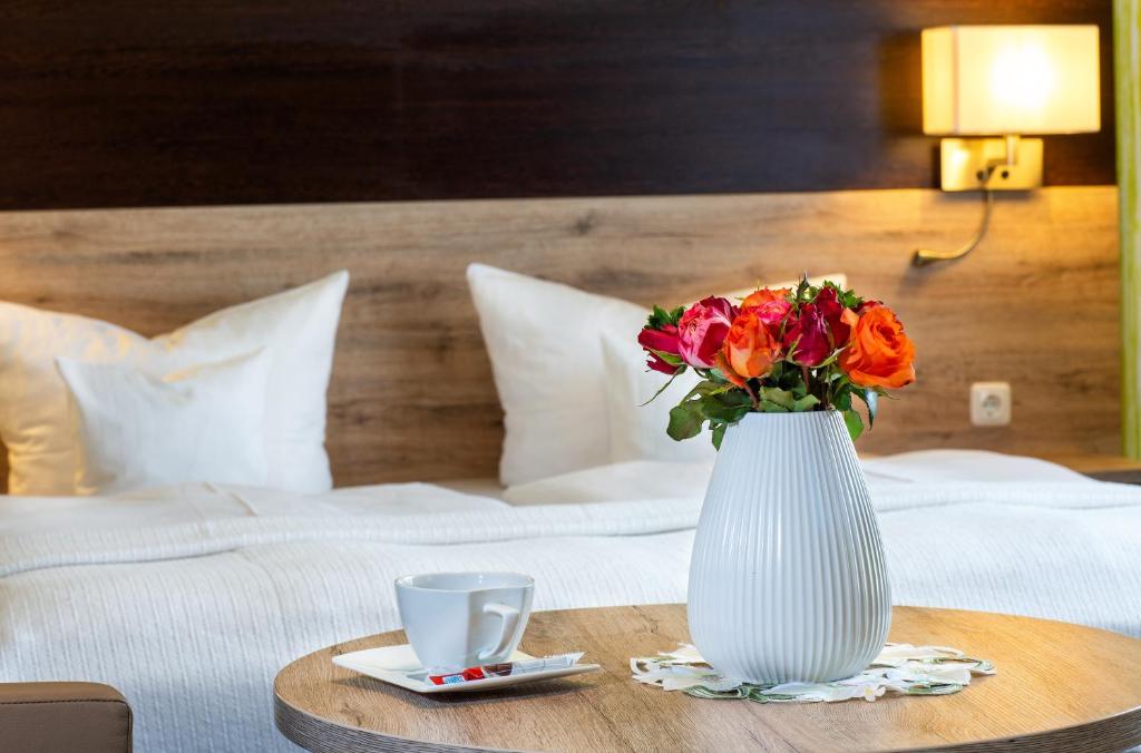 a white vase with flowers on a table next to a bed at Appart Hotel Roßdorf in Roßdorf