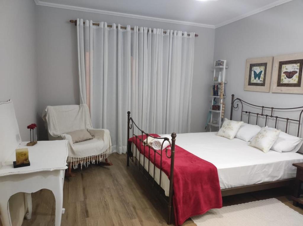 a bedroom with a bed with a red blanket and a chair at Refúgio da família - serra & lago in Guapimirim