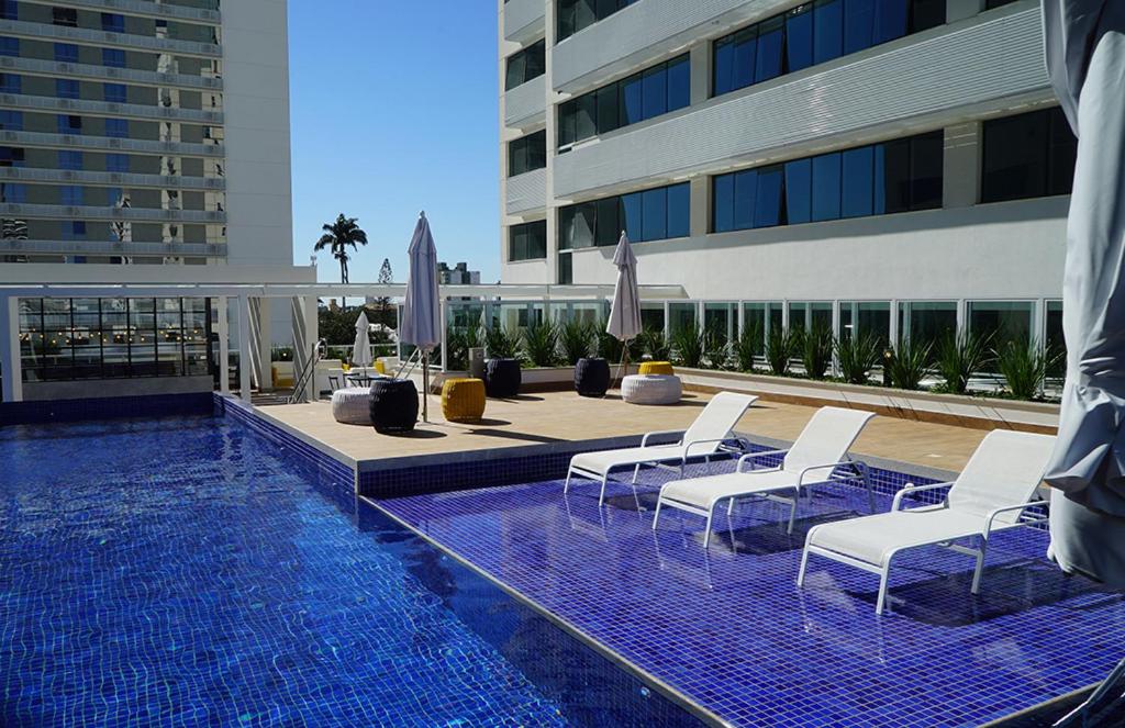 uma piscina com cadeiras brancas e um edifício em Apart Hotel - América Residence Campos dos Goytacazes em Campos dos Goytacazes