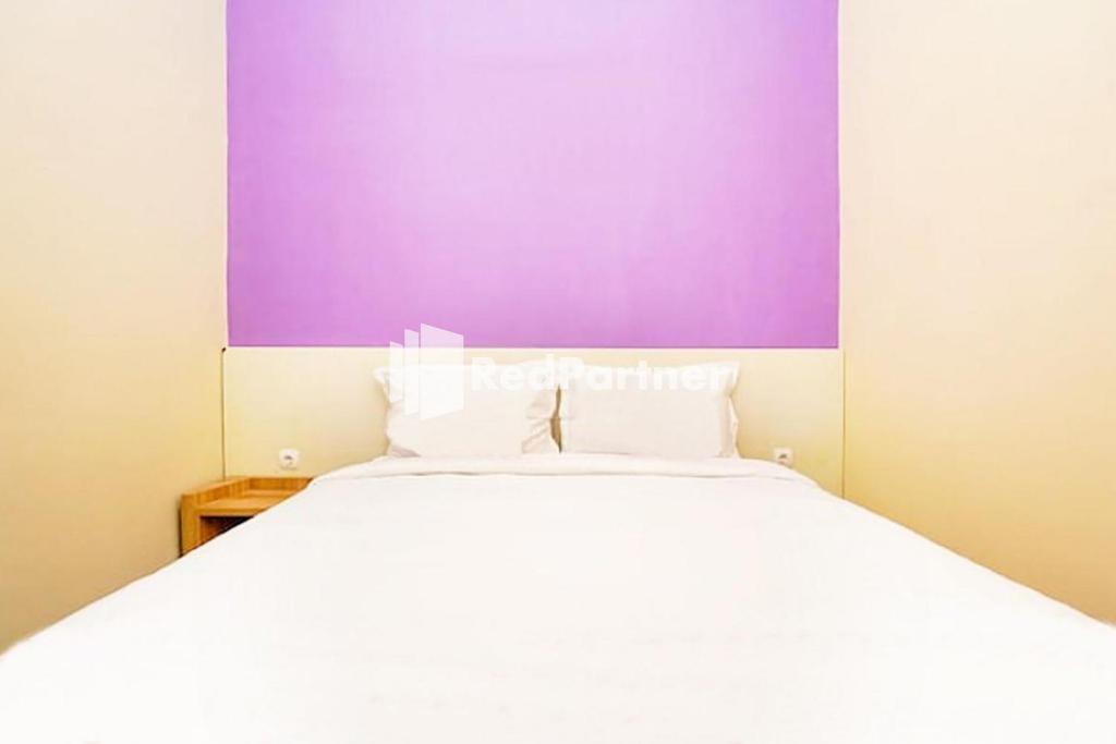 a bedroom with a white bed and a purple wall at Kupang Gunung Homestay Syariah near Islamic Center Surabaya Mitra RedDoorz in Surabaya