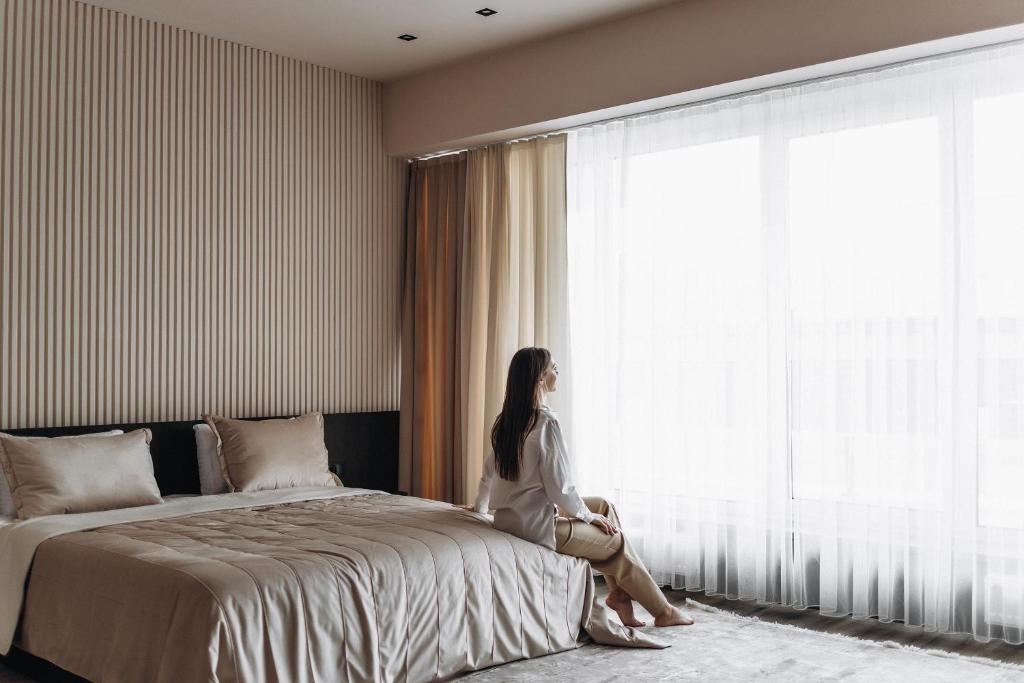 a woman sitting on a bed looking out the window at Garden plaza in Neresnytsya