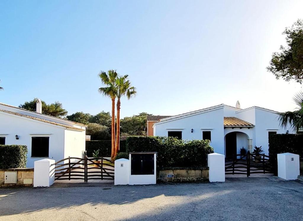 a white house with a gate and a palm tree at Villas El Pinar in Cala en Blanes