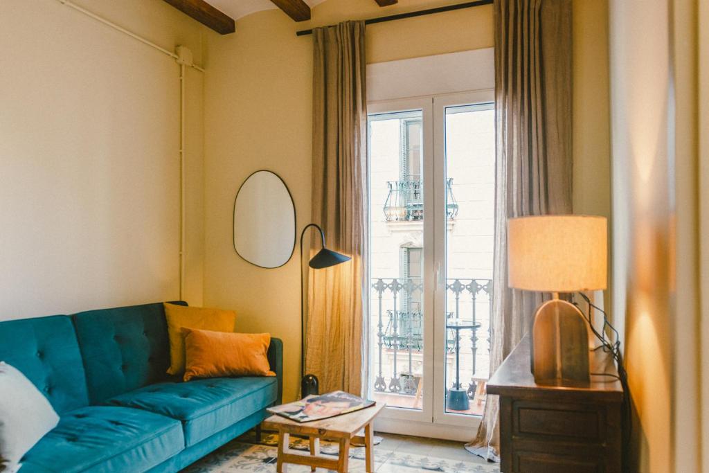 salon z niebieską kanapą przed oknem w obiekcie Brummell Apartments Montjuic w Barcelonie