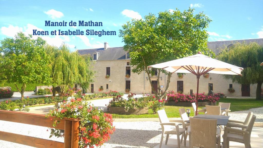 une table avec un parasol devant un bâtiment dans l'établissement Hôtel Le Manoir De Mathan Crépon à la campagne 5 mn d'Arromanches et 10 mn de Bayeux, à Crépon