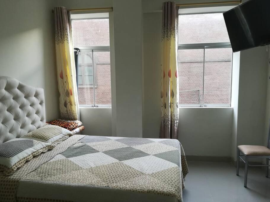 een slaapkamer met een bed met een geruite deken en 2 ramen bij Studio entero cerca al Palacio Gobierno in Lima
