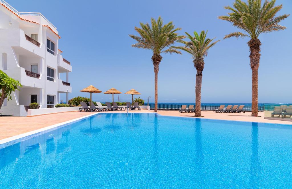 a swimming pool with palm trees and the ocean at Barceló Fuerteventura Royal Level in Caleta De Fuste