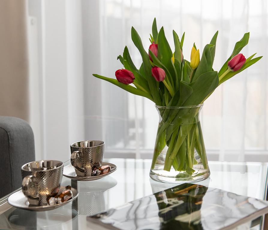 a vase of flowers on a glass table with two cups at Apartamenty Centrum II in Bydgoszcz