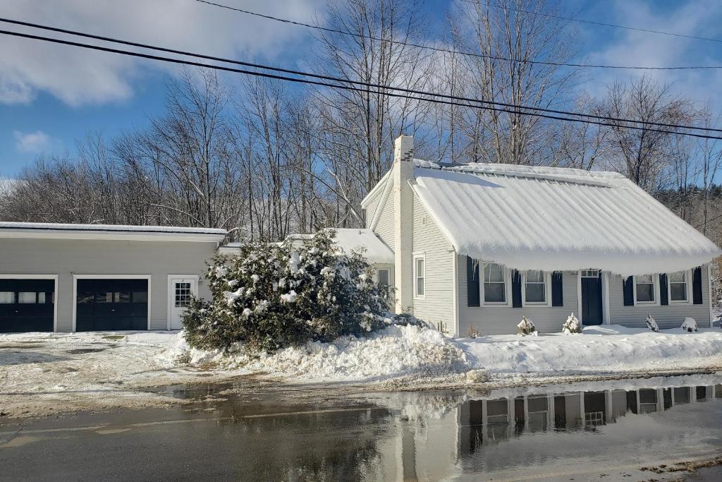 a white house in the snow with a reflection in the water at Vermont Farm in Proctorsville