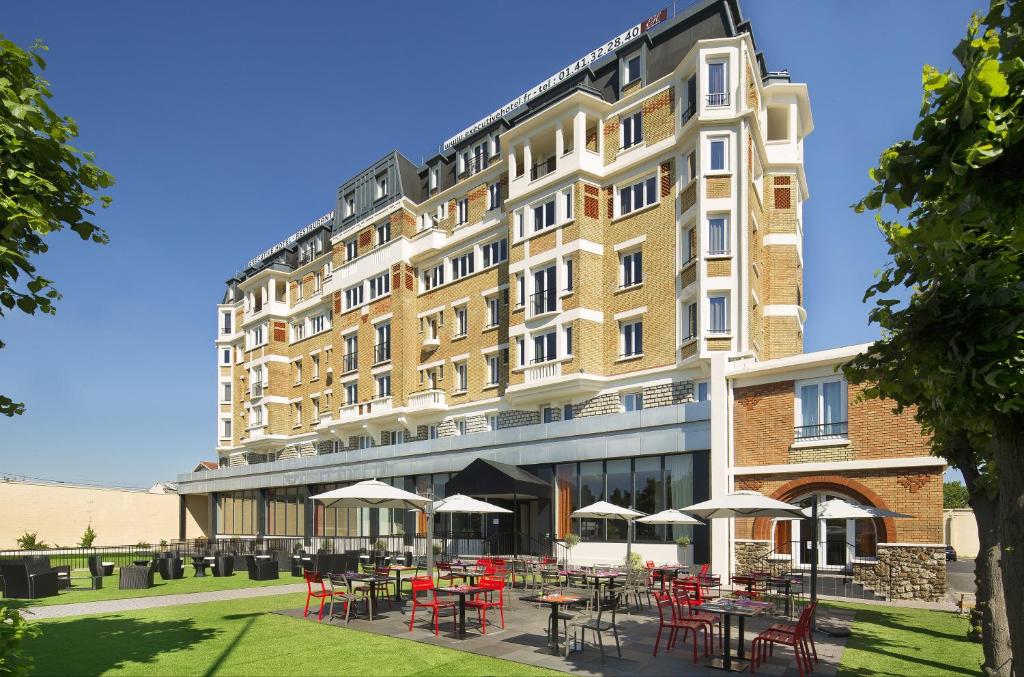 ein großes Gebäude mit Tischen und Stühlen davor in der Unterkunft Executive Hôtel Paris Gennevilliers in Gennevilliers