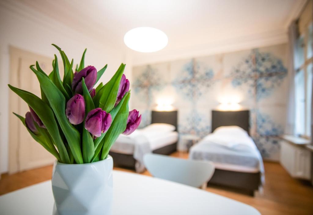 Aparthotel Villa Elon في فورث: إناء من زهور الأقحوان الأرجوانية في غرفة مع سريرين