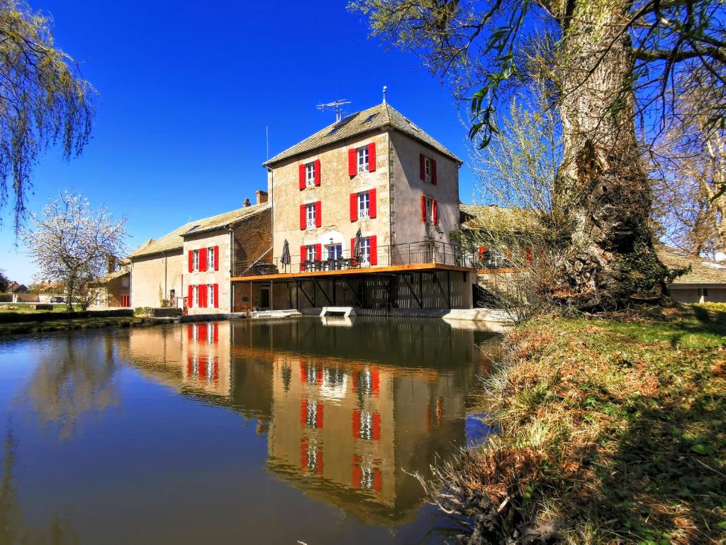 a building with red windows on the side of a river at Le Moulin des Ducs in Épinac-les-Mines