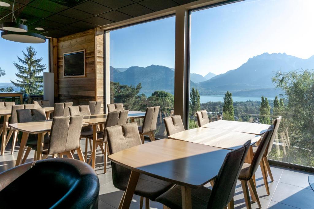 una sala da pranzo con tavoli, sedie e una grande finestra di Village Club Les Balcons du Lac d'Annecy - Neaclub a Sevrier