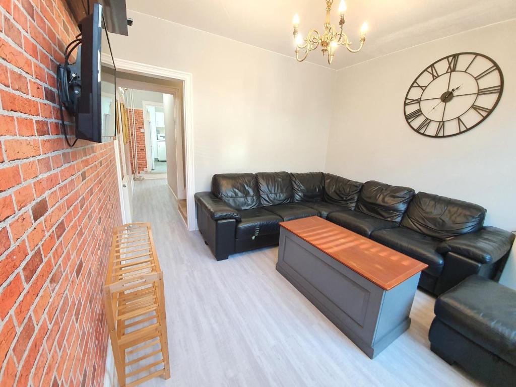 a living room with a black leather couch and a clock at Victorian Home, 3BR, Airport, M1, 6 beds, sleeps 12 in Luton