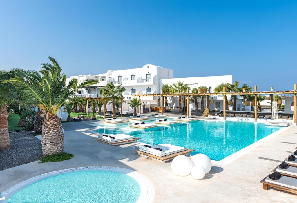 a large swimming pool with lounge chairs and palm trees at Smy Mediterranean White Santorini in Kamari
