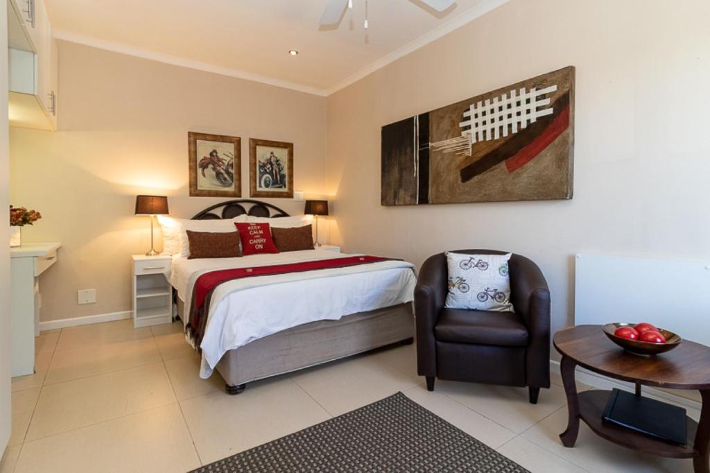 ein Schlafzimmer mit einem Bett, einem Stuhl und einem Tisch in der Unterkunft Tyger Classique Self-Catering Cape Town, Tyger Valley in Bellville