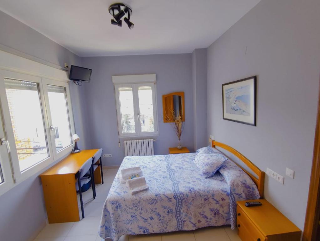 a bedroom with a bed and a desk and windows at Hostal Monteclaro in Ponferrada