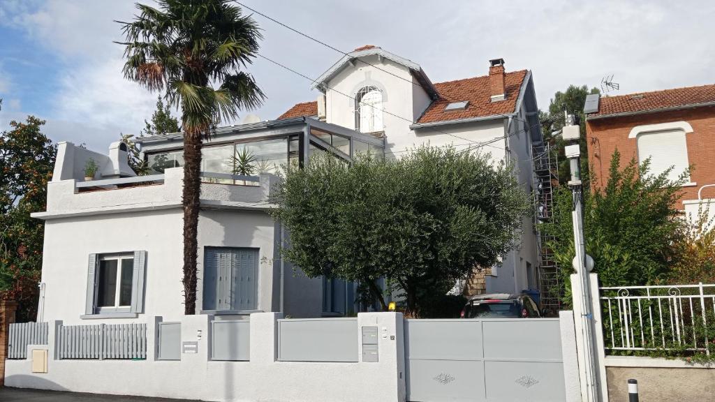 a white house with a white fence and a palm tree at Grand appartement indépendant, 4 personnes et plus, piscine et jardin in Toulouse