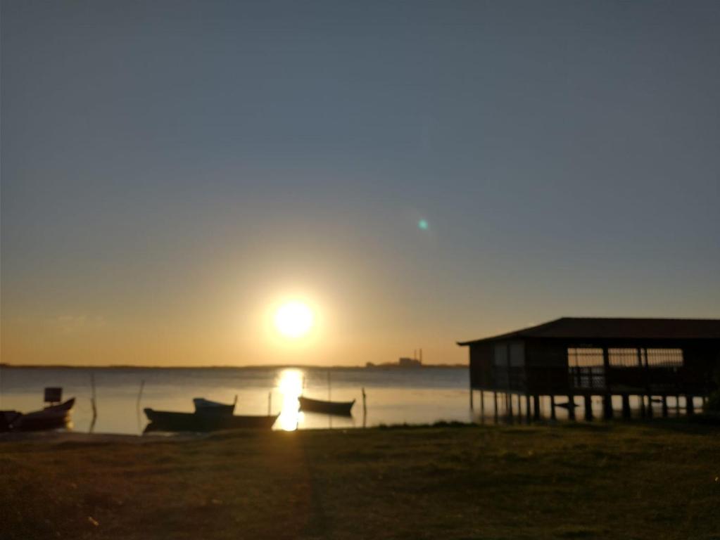 um pôr do sol na praia com uma casa e um barco em Suites em Cabo Frio em Cabo Frio