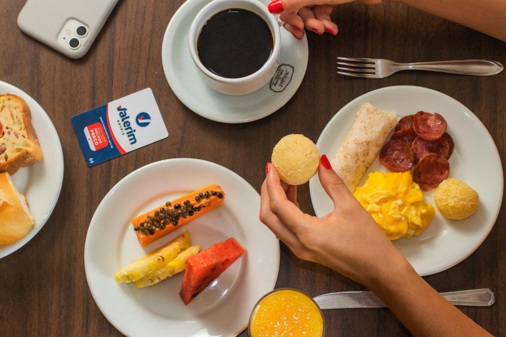 a table with plates of breakfast food and a person holding acookie at Hotel Valerim Itajaí / Navegantes in Itajaí