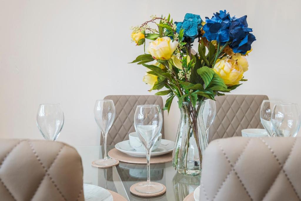 a glass table with a vase with blue and yellow flowers at Spacious 3-Bedroom House near ExCeL Free Parking E16 in London