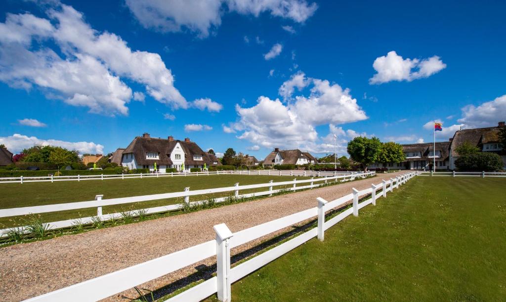 une clôture blanche dans un champ avec des maisons dans l'établissement Benen-Diken-Hof, à Keitum