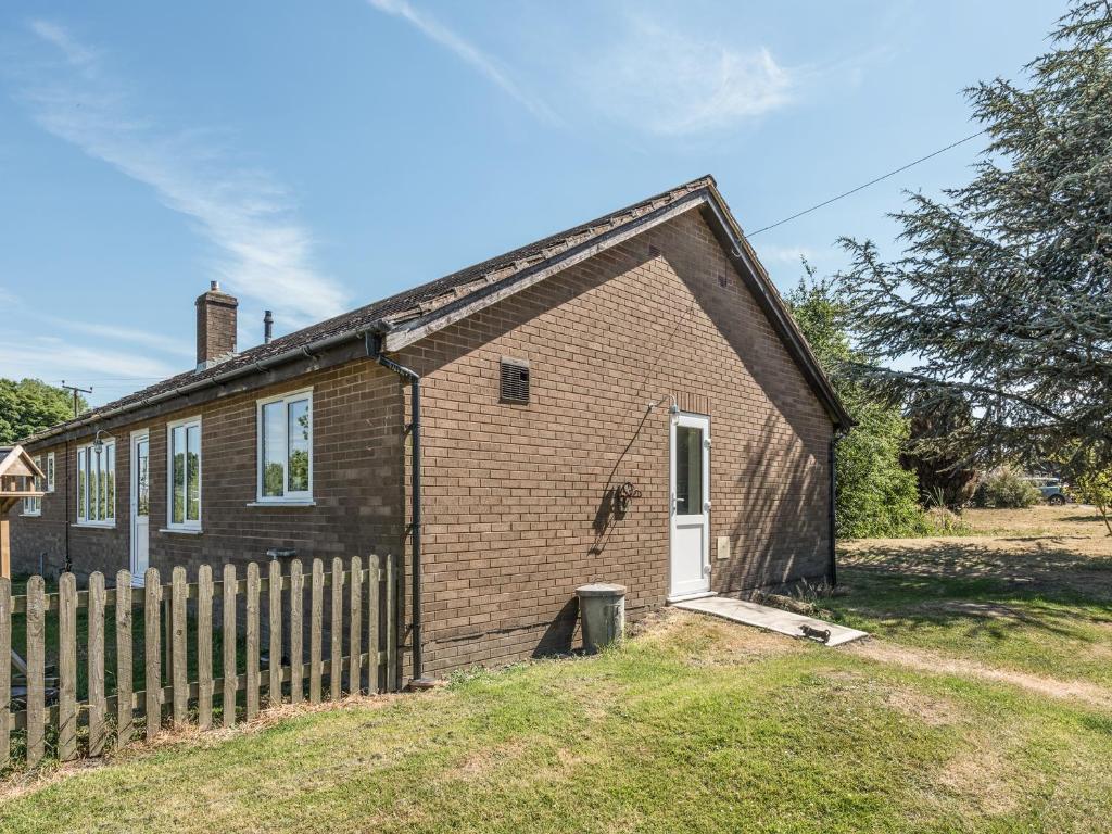 a small brick house with a wooden fence at The Bungalow in Cleobury Mortimer