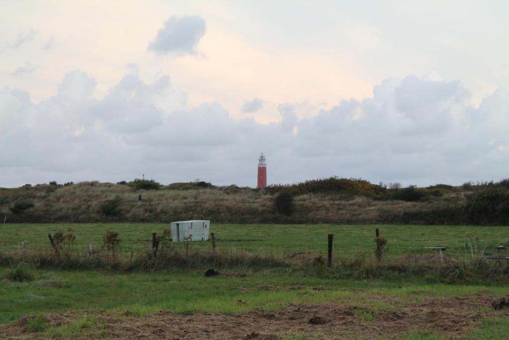 einen Leuchtturm auf einem Hügel mit einem Feld mit einem Zaun in der Unterkunft boerderij de duinen 115 in De Cocksdorp