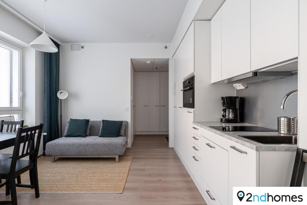 a kitchen with white cabinets and a table and a couch at 2ndhomes Tampere "Areena" Apartment in Tampere