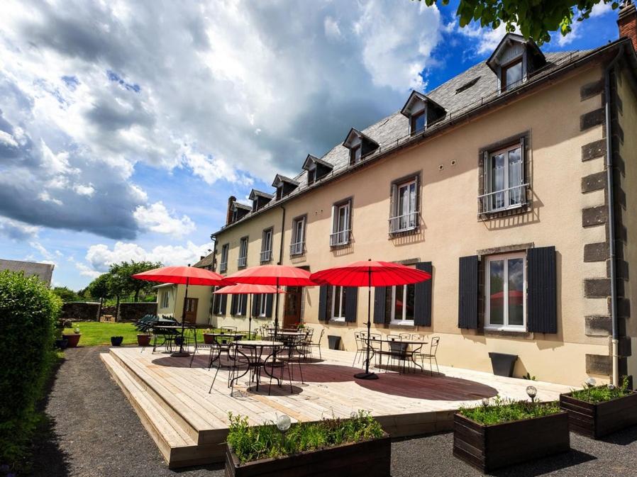 un bâtiment avec des tables, des chaises et des parasols rouges dans l'établissement Le Clos Auvergnat, à Tauves